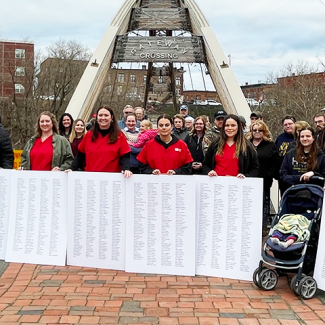 Group of nurses in front of "Gateway Crossing" bridge with huge print out of petition signatures