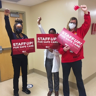 Three nurses with raised fists hold signs "Staff Up for Safe Care"