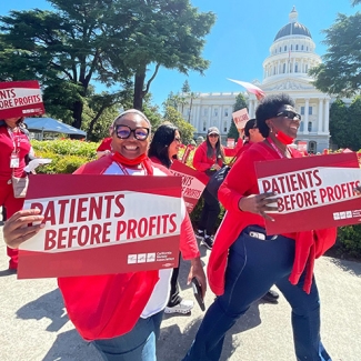 Nurses marching in front of California Capitol building holding signs "Patients Before Profits"