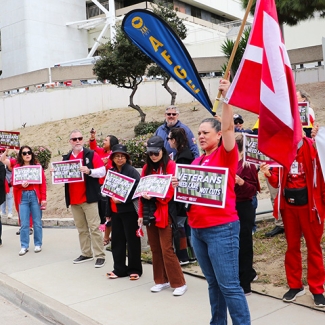 Nurses rallying in front of hospital, holding signs "No Cuts: A Healthy VA = Healthy Vets"