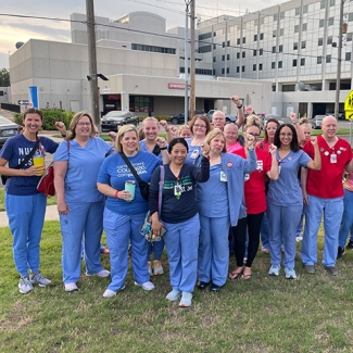 Large group of nurses outside hospital with raised fists