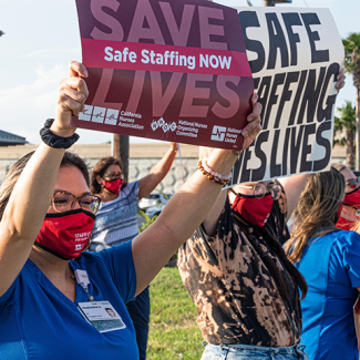 Corpus Christi nurses holding signs on street "Save lives: Safe staffing now" and "Safe staffing saves lives"