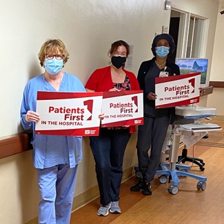 Three nurses inside hospital hold signs "Patients First"