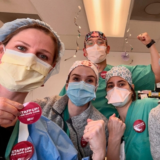 Group of nurses inside hospital hold raised fists