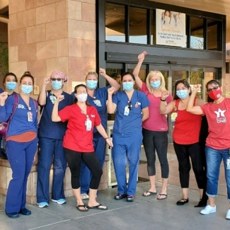 Large group of nurses outside hospital with raised fists