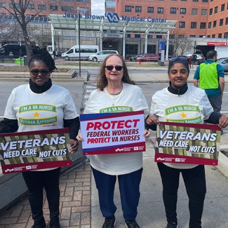 Three nurses outside hospital holding signs "Veterans Need Care Not Cuts" and "Protect Federal Workers"
