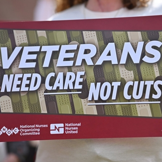 Hands holding sign "Veterans Need Care Not Cuts"