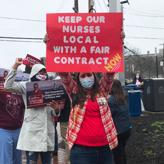 Nurse outside hospital holds sign "Keep nurses local with a fair contract now!"