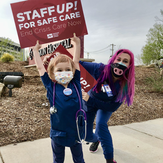 Child in scrubs with stethoscope holding sign: Staff up, end crisis care now