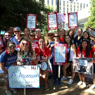 Large group of nurses hold signs demanding better treatment of nurses and patients by Ascension