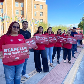 Group of four nurses outside hospital hold signs "Staff up for safe patient care"