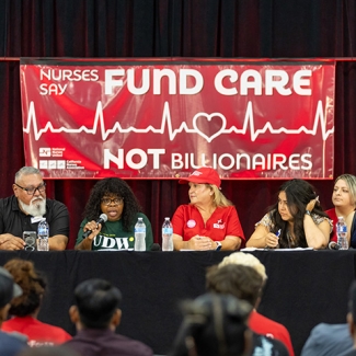 Panel at town hall in front of banner "Fund Care Not Billionaires"