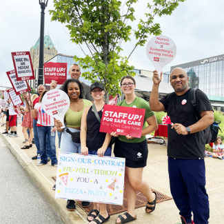 Nurses in front of Saint Louis University Hospital holding signs like "Staff up for safe care!"