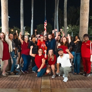 Large group of nurses outside, smiling, with raised fists