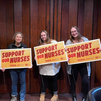 Four nurses inside holding signs "Support Our Nurses"