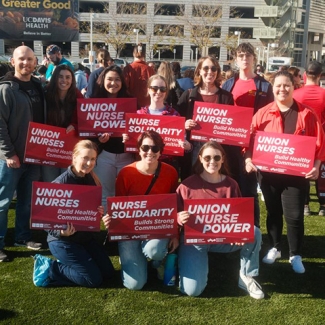 Group of nurses outside, smiling, holding signs "Union Nurse Power"