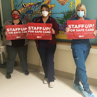 Three Monterey County RNs holding signs in hall "Staff up for safe care. End crisis care now."