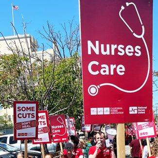 Marching on sidewalk with signs "Nurses care" (stethoscope image) and "Some cuts don't heal" (bandaid image)