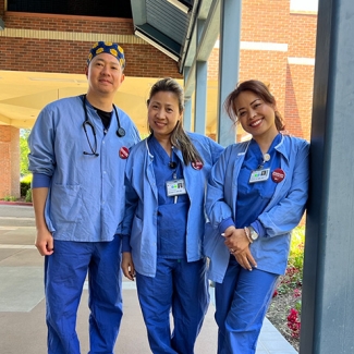 3 nurses in blue scrubs outside standing side-by-side, smiling