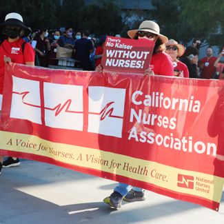 Nurses marching and holding CNA/NNU banner and signs at LAMC: "There's no Kaiser without nurses!"