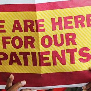 Nurse holding up sign that reads "We are here for our patients."