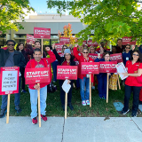 Large group of nurses outside hospital holding signs "Staff Up for Safe Patient Care"