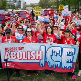 Large group of nurses outside, holding banner "Nurses Say Abolish ICE"