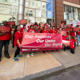 Group of nurses outside, holding banner "Our Patients, Our Union, Our Rights" and signs "Union Busting is a Sin"