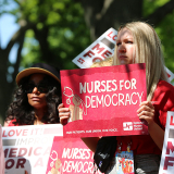 Nurse outside, holding sign "Nurses for Democracy"