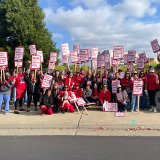 Large group of nurses outside holding signs "Kaiser: Put Patients Over Profit" and "Nurses at the Bedside, Kaiser at the Bank"
