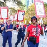 Nurses on picket line outside of hospital, smiling, holding signs about being on strike.