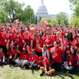 Large group of nurses outside capitol building, smiling, with raised fists
