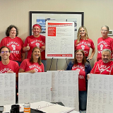 Group of nurses inside, holding large printouts of contract signers