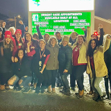 Large group of nurses outside hospital, smiling, with raised fists