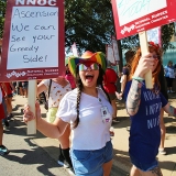 Nurses on picket line, one holds sign "Ascension, we can see your greedy side"