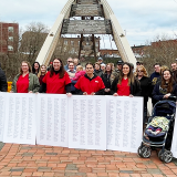 Group of nurses in front of "Gateway Crossing" bridge with huge print out of petition signatures