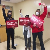 Three nurses with raised fists hold signs "Staff Up for Safe Care"