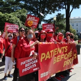 Group of nurses marching towards CA Capitol building, holding banner "Patients over Profits"
