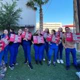 Large group of nurses in blue scrubs outside hospital holding signs "HCA Put Patients Over Profits"
