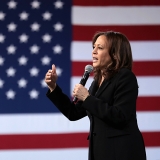 Vice President Kamala Harris speaking into microphone in front of American flag