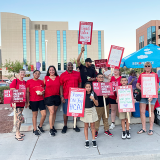 Nurses and their kids holding signs in front of hospital "Shame on you HCA!", "HCA, Put patients over profits!", "Proud union nurses!"