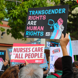 Hands holding signs "Transgender Rights Are Human Rights" and "Nurses Care for All People"