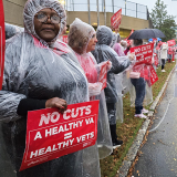 Nurses standing in rain along street with signs: "No cuts: A healthy VA = healthy vets"