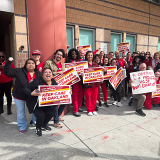 Large group of nurses holding signs "Keep care in Oakland"