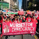 Nurse marching in street holding banner "Nurses for Democracy"