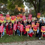 Large group of nurses outside holding signs "Safe Staffing NOW", "Recruit, Retain, Respect RNs", and "Nurses are the heart of patient care"