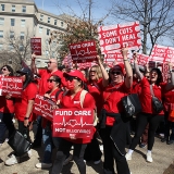 Nurses marching holding signs "Some Cuts Don't Heal" and "Fund Care Not Billionaires"