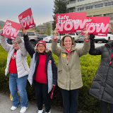 Nurses outside hospital holding signs "Safe Staffing Now" and "Fair Contract Now"