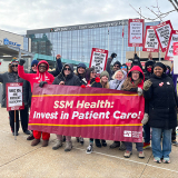 Group of nurses outside hospital, smiling, raised fists, holding banner "SSM Health: Invest in Patient Care"